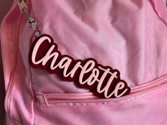 Pink backpack with a 'Charlotte' keychain attached Maroon Outline and Pink Name